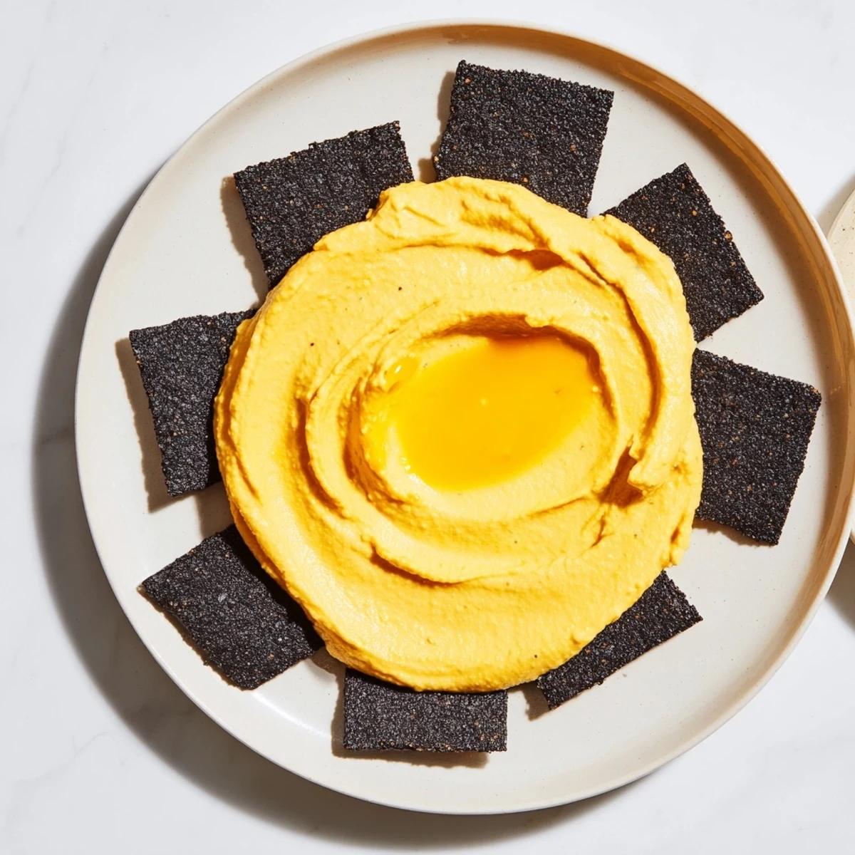 Charcoal crackers arranged as a dark circle with creamy The Midnight Sun carrot dip at the center.