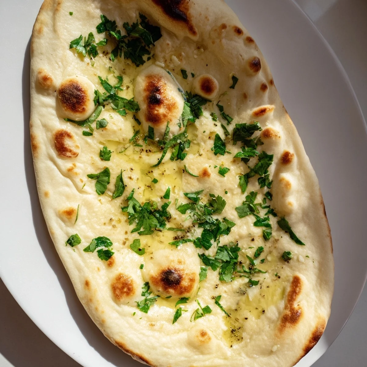 Freshly made Homemade Garlic Naan, soft and pillowy, with visible bubbles and flecks of garlic.
