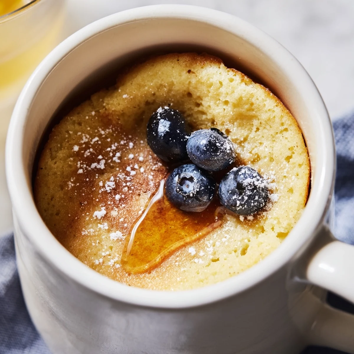 Golden, fluffy microwave mug pancakes topped with sweet maple syrup and fresh berries for breakfast.