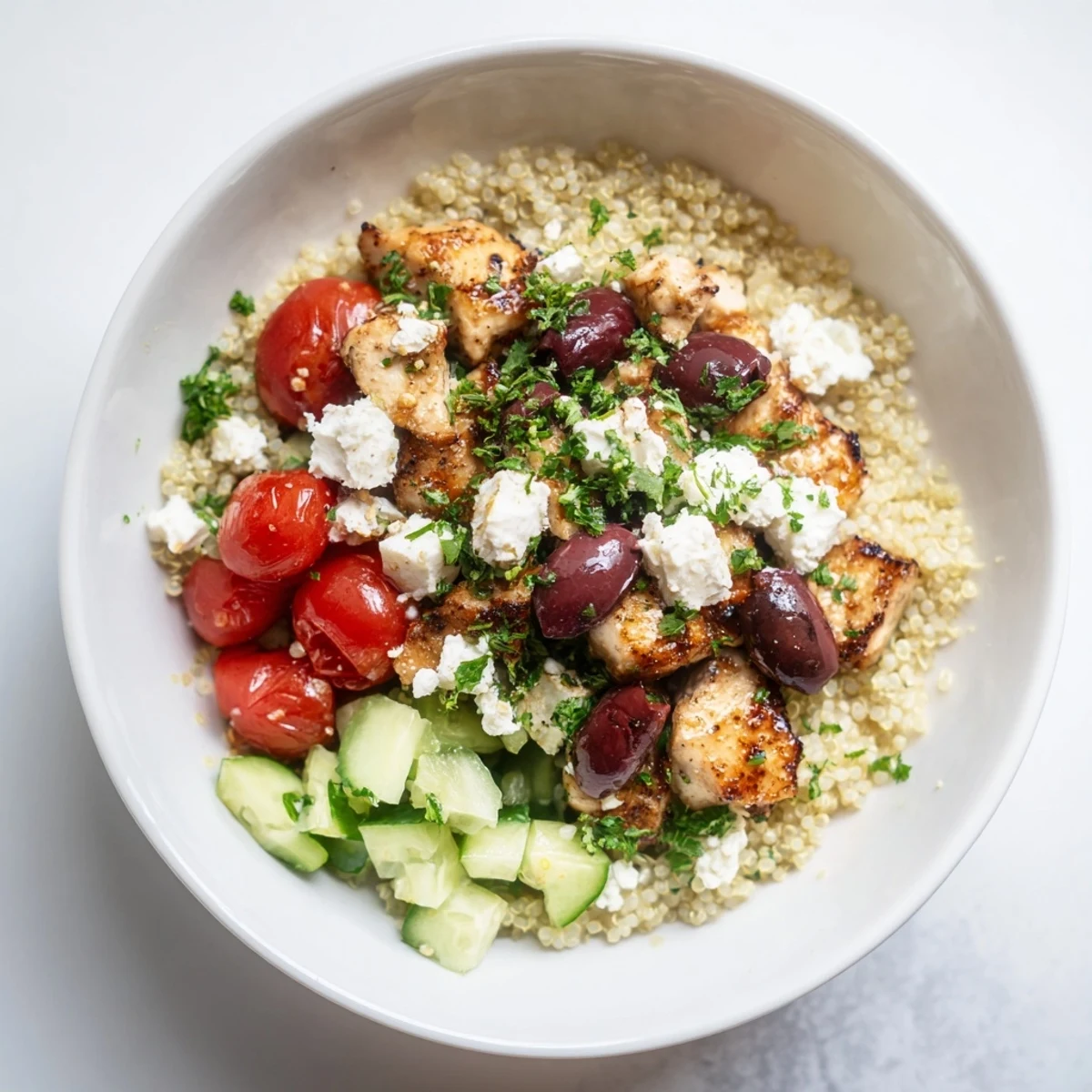 Juicy grilled chicken, creamy feta, olives, chickpeas, and crisp veggies on fluffy quinoa in a Mediterranean Chicken Bowl, drizzled with tangy lemon-oregano dressing.