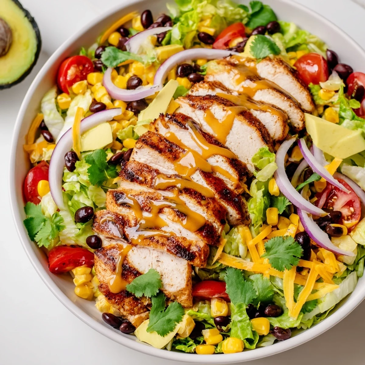 Freshly grilled honey lime chicken slices rest atop a vibrant bed of romaine, corn, black beans, and avocado in this Taco Salad.  