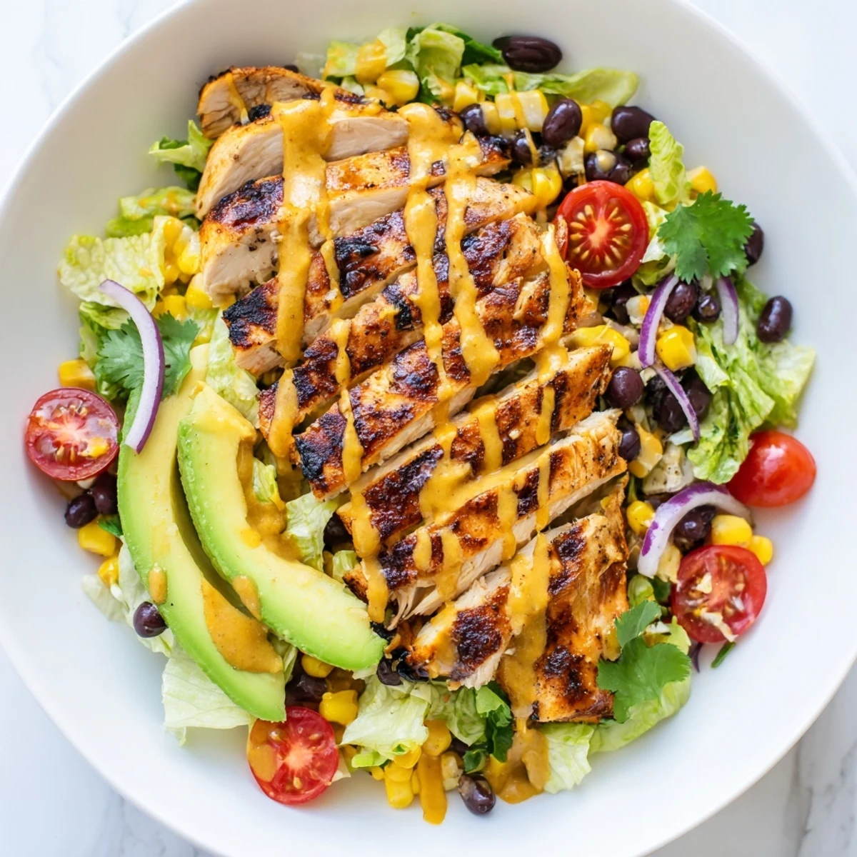 A close-up of honey lime chicken taco salad with charred chicken, diced avocado, and drizzled dressing for a zesty finish.