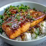 Hot teriyaki salmon rests on steamed rice, surrounded by colorful stir-fried peppers, carrots, and tender broccoli florets.