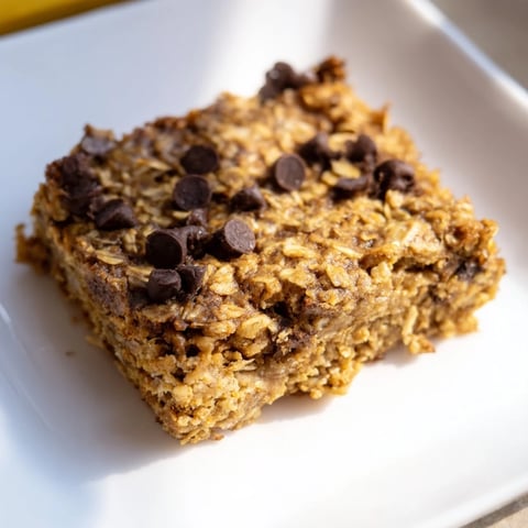 A square of Baked Oats That Taste Like Cake, golden brown with melted chocolate chips, ready to slice.