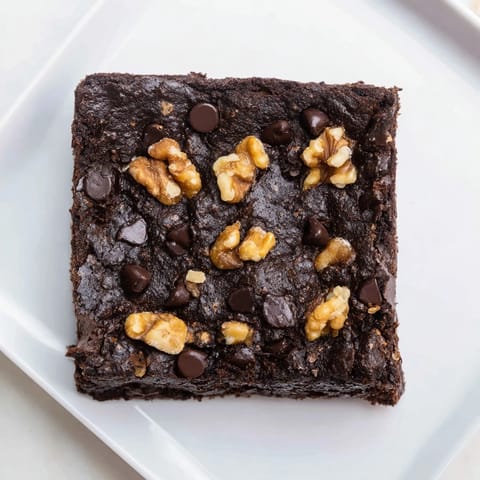 A close-up of rich, chocolate-laden Fudgy Walnut Brownies dotted with walnuts, ready to be cut and served.