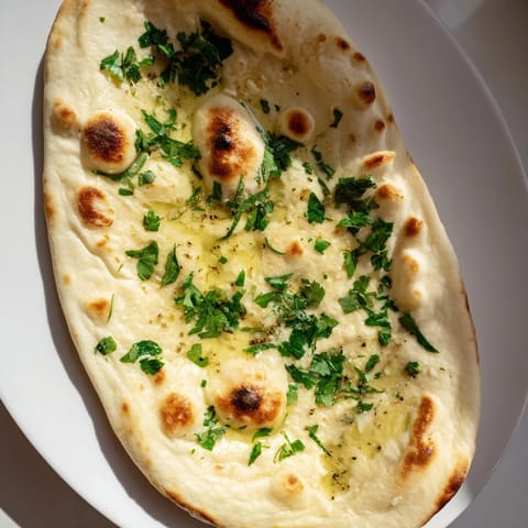 Freshly made Homemade Garlic Naan, soft and pillowy, with visible bubbles and flecks of garlic.