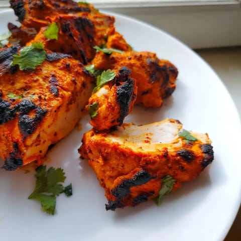 Golden-brown Indian Tikka Spiced Chicken pieces on a wire rack, roasted to crispy perfection with charred edges.