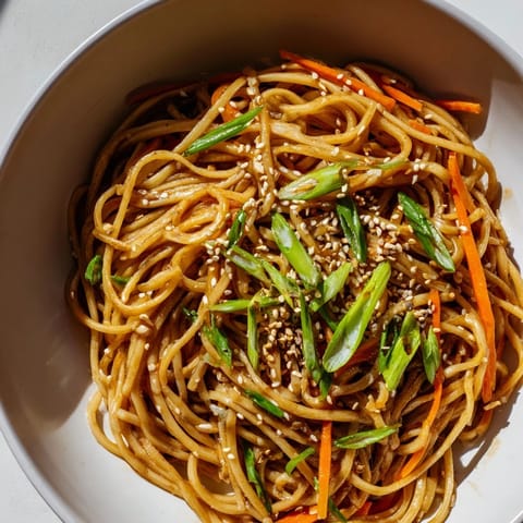 A close-up of Asian Garlic Noodle Bowl topped with crisp bean sprouts, julienned carrot, and optional red chili slices.  