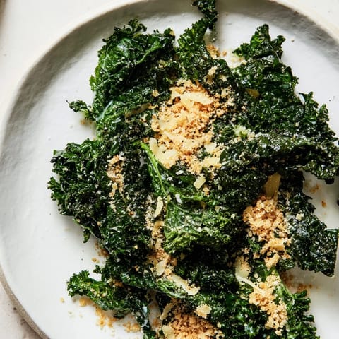 A vibrant Garlic Parmesan Kale Salad served in a white bowl with shaved cheese and cracked black pepper.