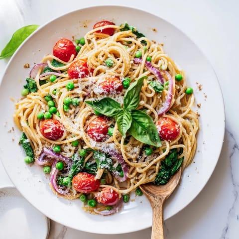 A vibrant pan of Spring Veggie One-Pot Spaghetti features halved cherry tomatoes, garlic, and melty Parmesan ready to serve.