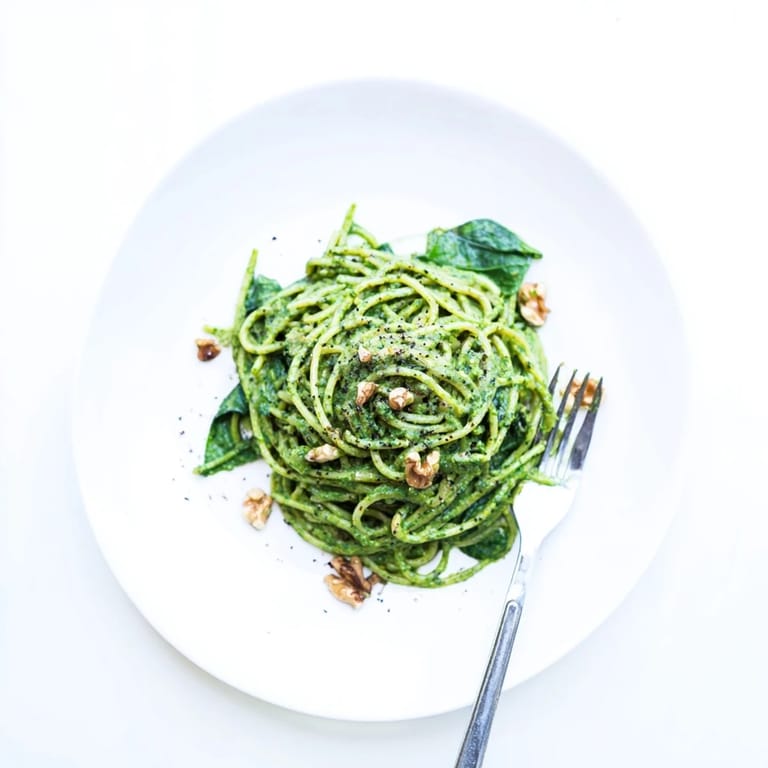 Serving suggestion for Creamy Spinach Walnut Pasta, a luscious plant-based main course topped with chopped walnuts and fresh herbs.