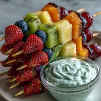 Rainbow Fruit Skewers with Honey Dip: Colorful fruit skewers arranged in a vibrant rainbow pattern, served with a creamy honey-yogurt dip for a refreshing summer snack.